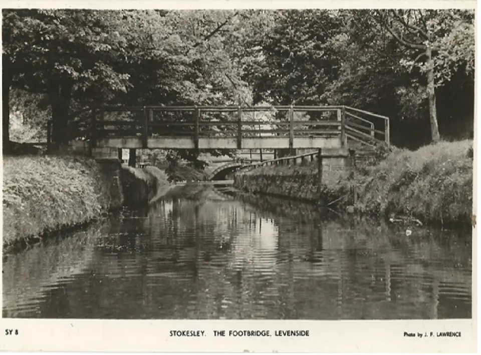 Old postcard of a footbridge with railings over a tree-lined stretch of river.