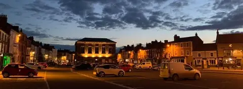 Stokesley High Street at dusk, with lit shopfronts and the Town Hall.
