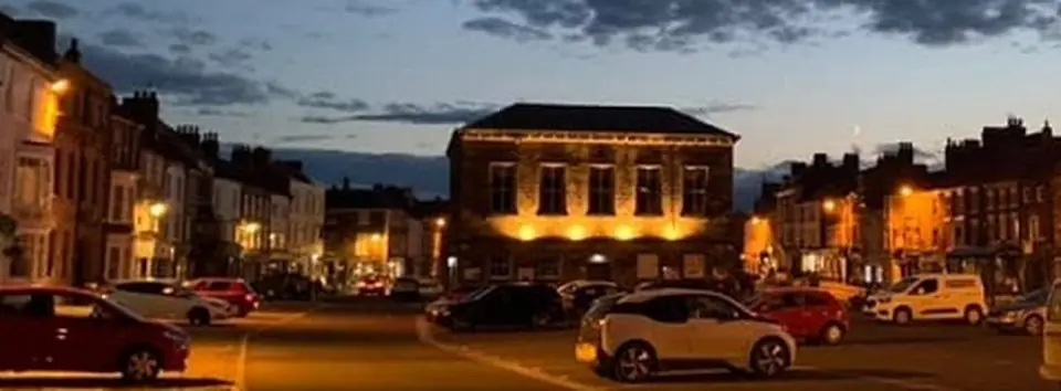 The Town Hall at dusk today, lit up, with parked cars in front.