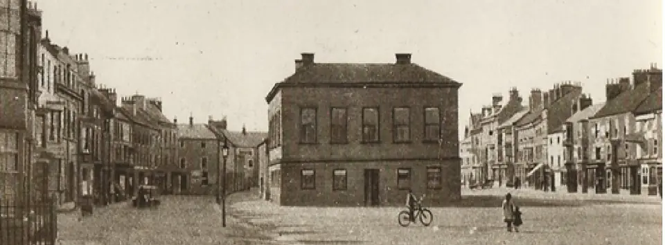 Old photograph of the Town Hall, a square brick building, on an open cobbled area with a cyclist in the foreground.