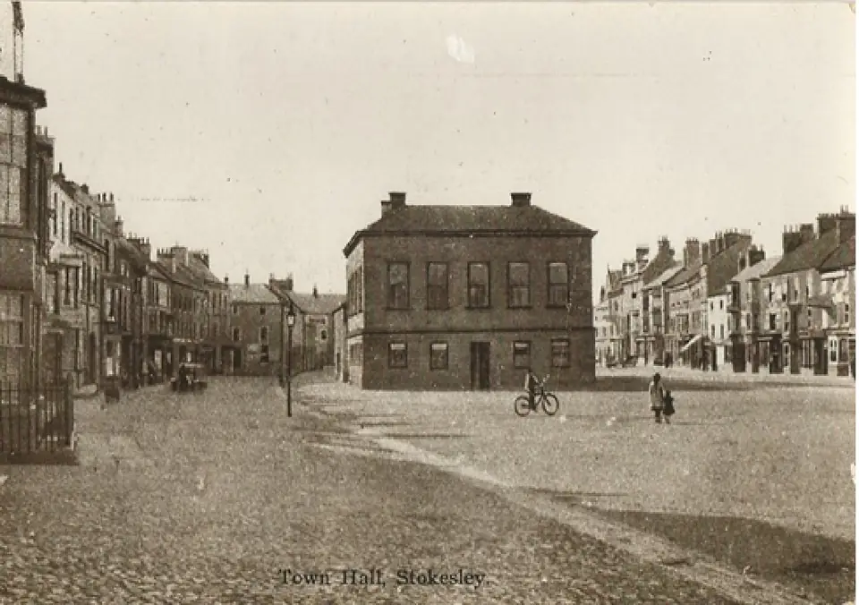 Old photograph of the Town Hall, a square brick building, on an open cobbled area with a cyclist in the foreground.